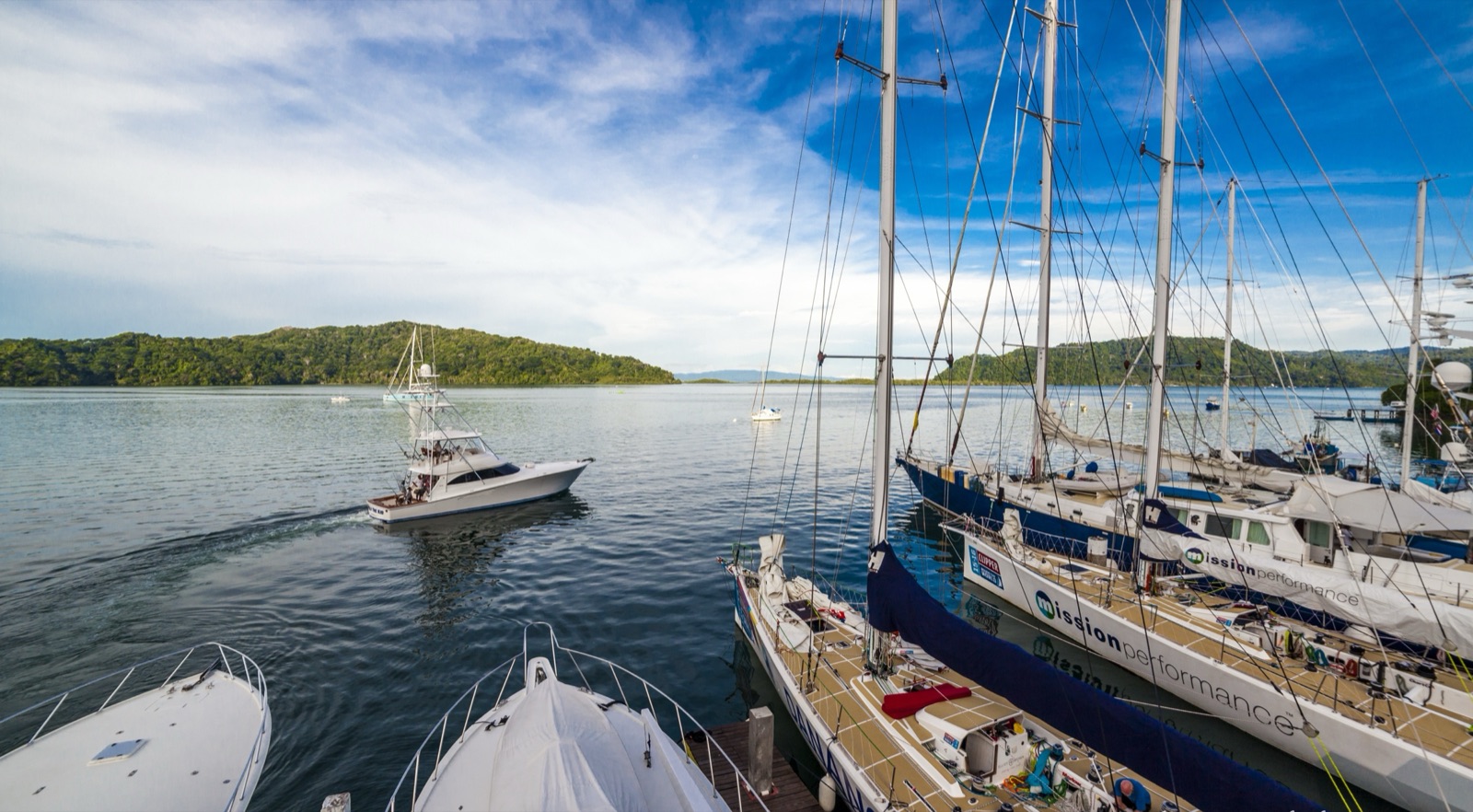 Sailing yachts and sportfishing boats in the slips at Banana Bay Marina, with a sportfishing boat heading out across Golfito Bay