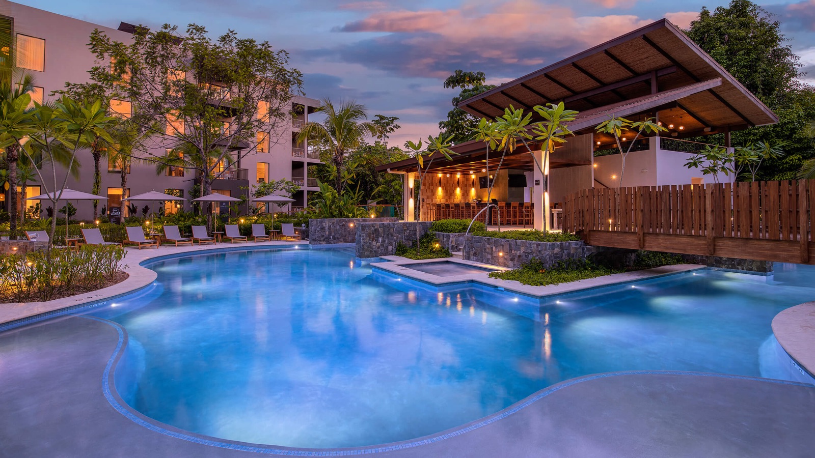 The lagoon pool at Botánika Osa Peninsula at dusk, with the resort's lit buildings behind