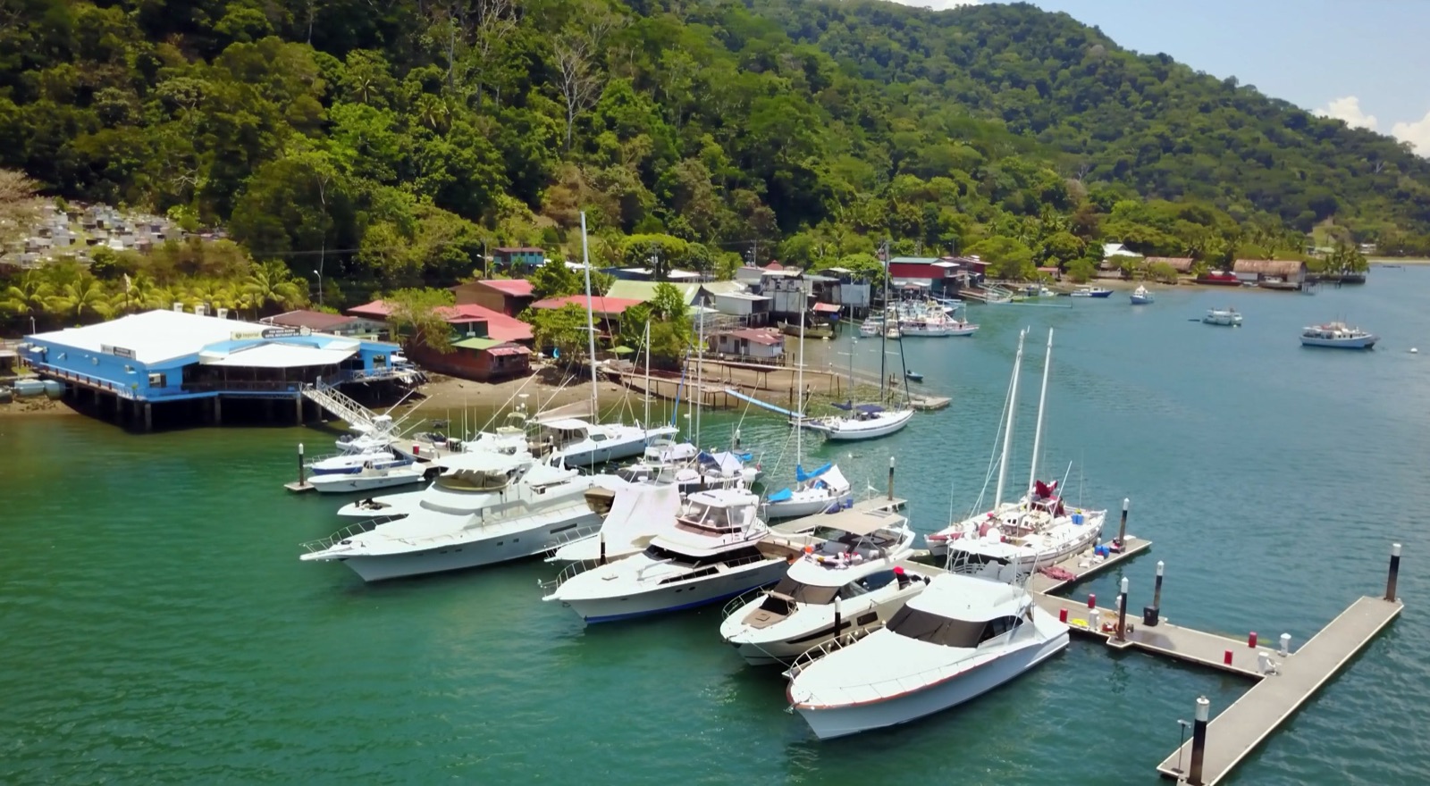 Aerial view of Fish Hook Marina & Lodge in Golfito, with its blue waterfront building and motor yachts and sailboats tied to the docks