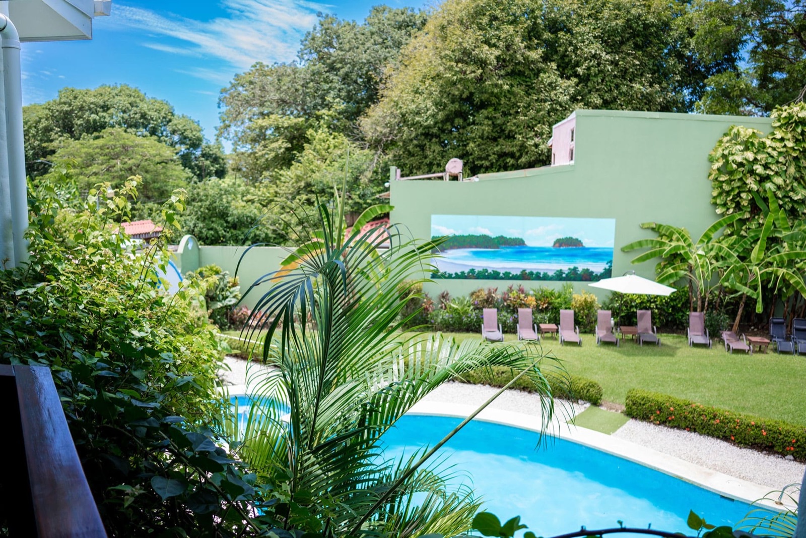 The pool and lawn with sun loungers at Hotel Giada in Sámara, below a garden wall painted with a beach mural