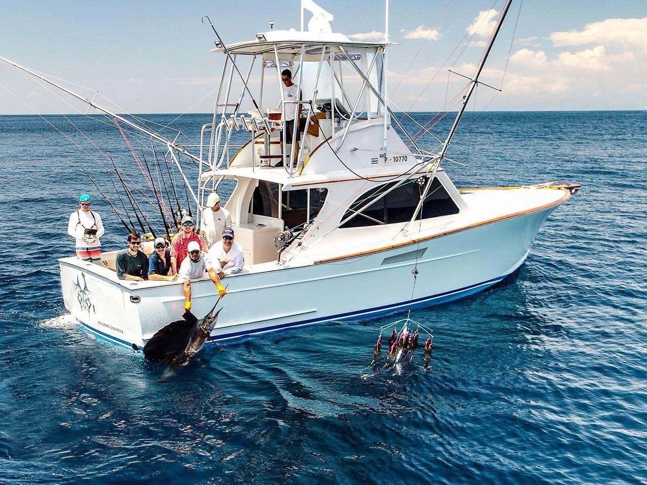 Anglers in the cockpit of the 38-foot custom sportfisher Tres Amigos, from the Jaco Tour Sportfishing fleet, with a sailfish alongside the boat