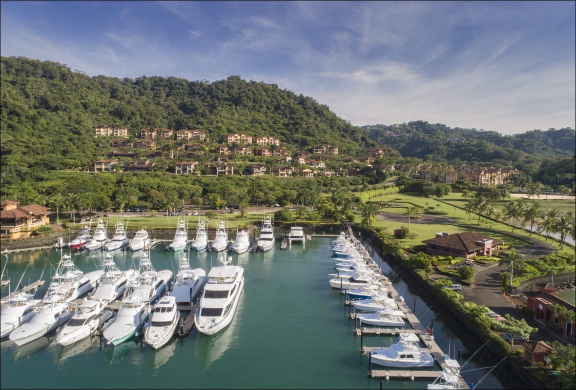 Aerial view of Los Sueños Marina in Herradura Bay, with rows of sportfishing yachts at the docks below forested hills and resort buildings