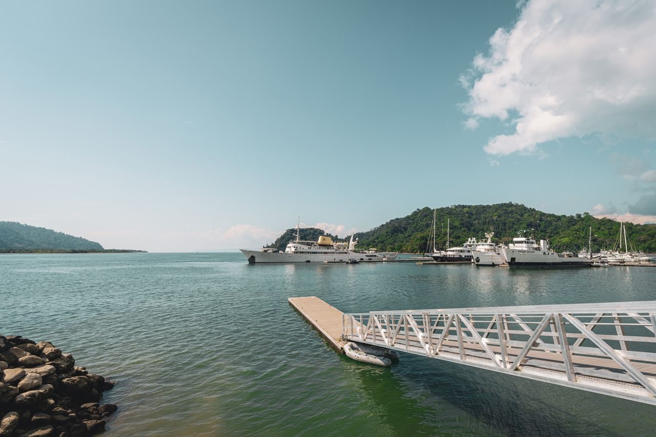 A gangway leading down to the floating docks at Marina Bahía Golfito, with large yachts berthed across the water