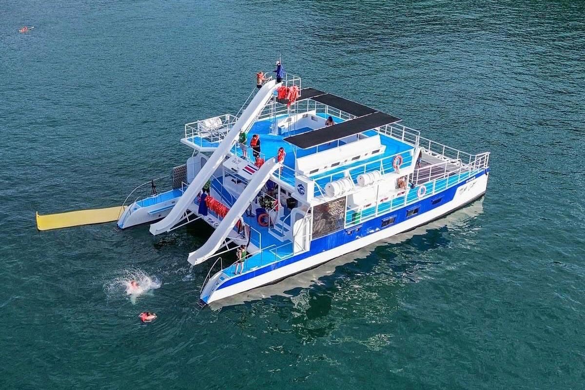 Aerial view of a Planet Dolphin catamaran at anchor off Manuel Antonio, with guests on deck and swimmers near its two water slides