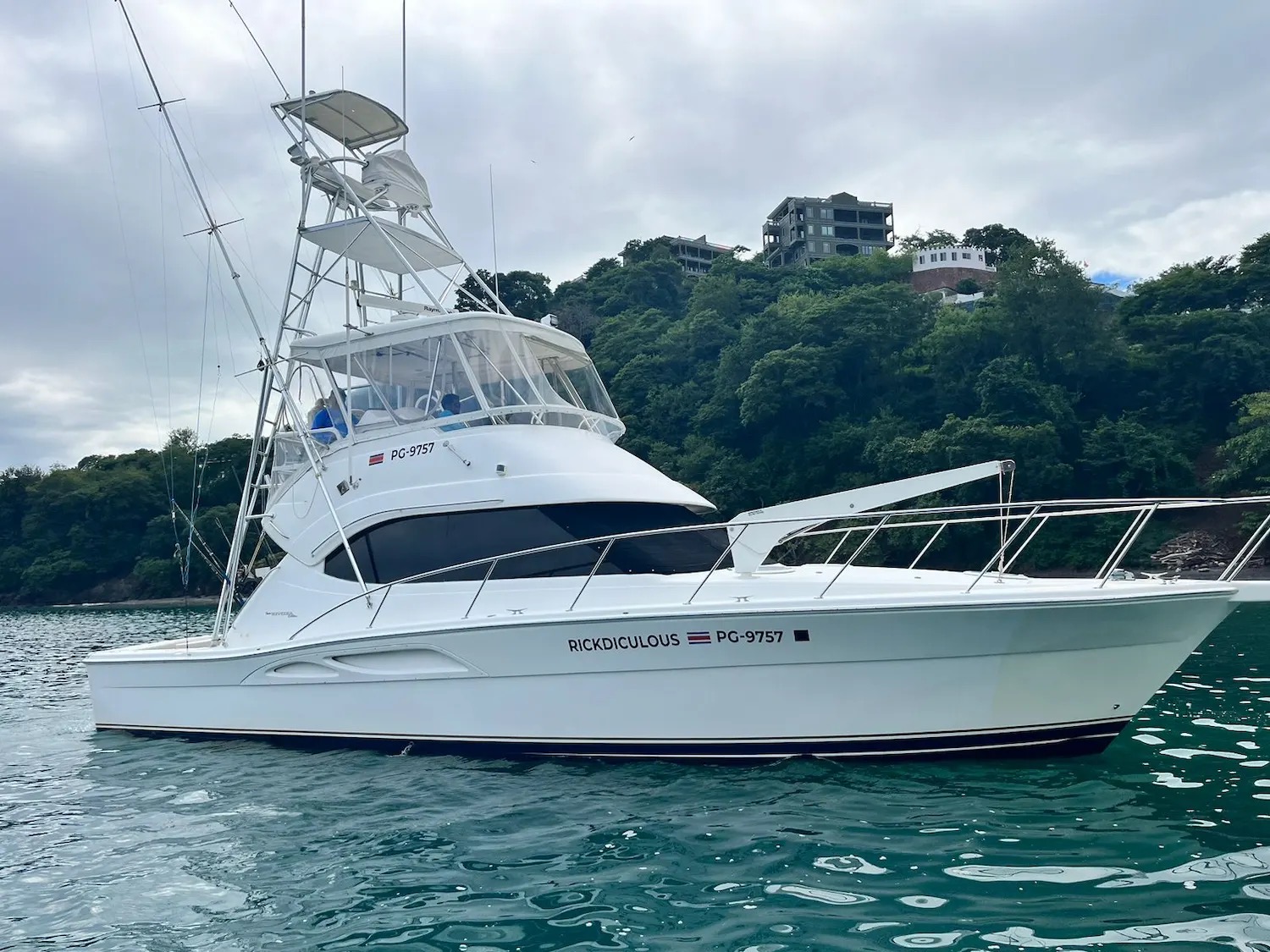 Yellowfin Sportfishing's 43-foot Riviera Rickdiculous at anchor below a wooded hillside, its tower and flybridge rigged for fishing